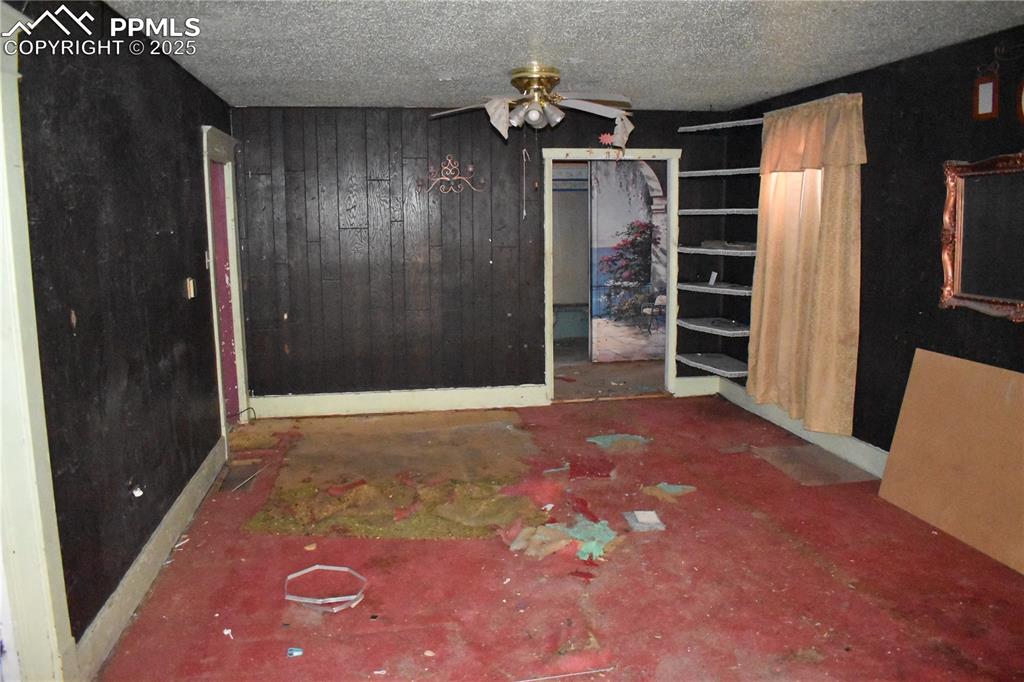 Image 13 of 23: Unfurnished bedroom featuring wood walls, a textured ceiling, a ceiling fan