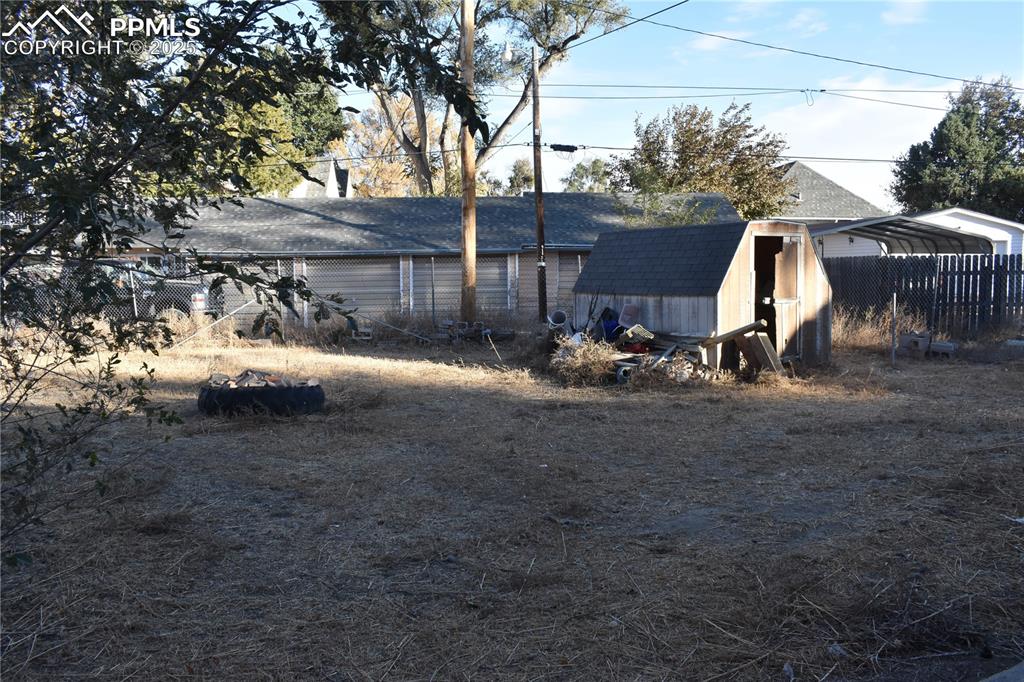 Image 4 of 23: Back of house with a storage unit and a shingled roof