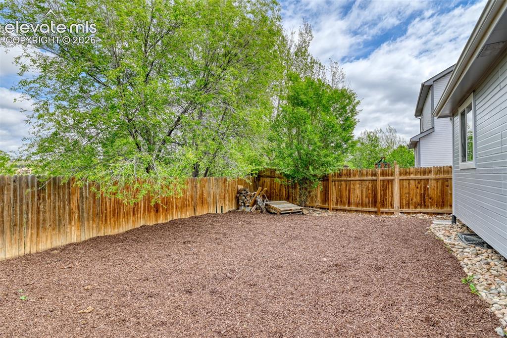 Image 10 of 40: Private backyard featuring wood chip ground cover and a perimeter wood fenc