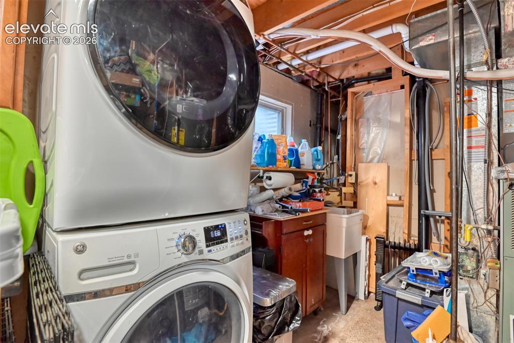 Image 40 of 40: Laundry area featuring a stackable washer and dryer, utility sink, and wood