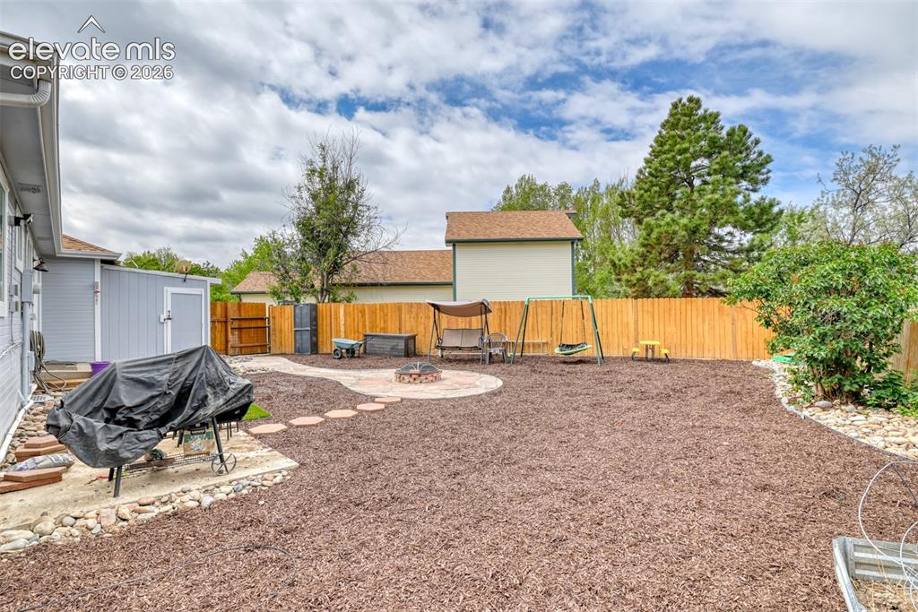 Image 9 of 40: Fenced backyard featuring a wood chip ground cover, stone pathway, and buil