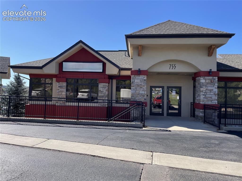 Caption: Stucco and stone facade with a prominent arched entry, dual glass-panel doors, dark-framed windows, 