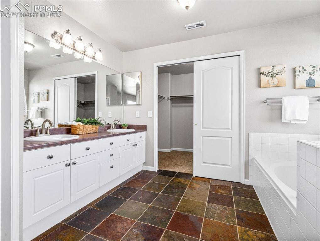 Image 18 of 23: Full bath with double vanity, a spacious closet, dark stone finish flooring