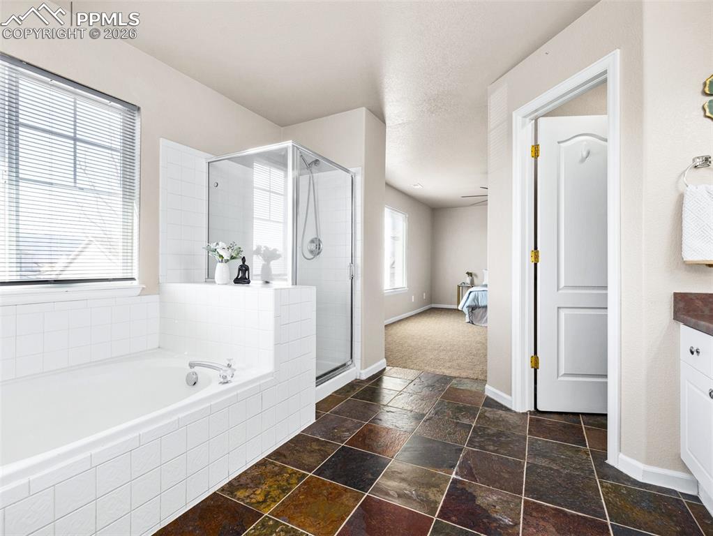 Image 19 of 23: Bathroom featuring a stall shower, stone tile flooring, a garden tub, and v