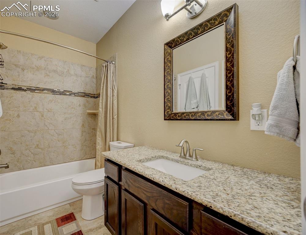 Image 26 of 30: Full bath with vanity, a textured wall, shower / bath combo, and toilet