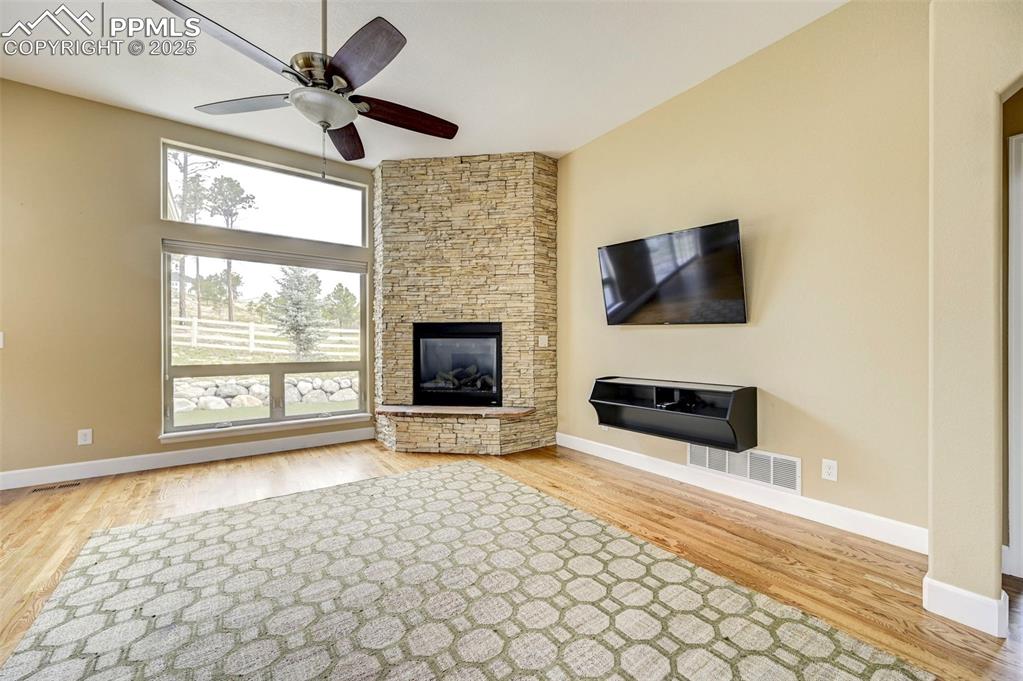 Image 5 of 30: Unfurnished living room with ceiling fan, a stone fireplace, baseboards, wo