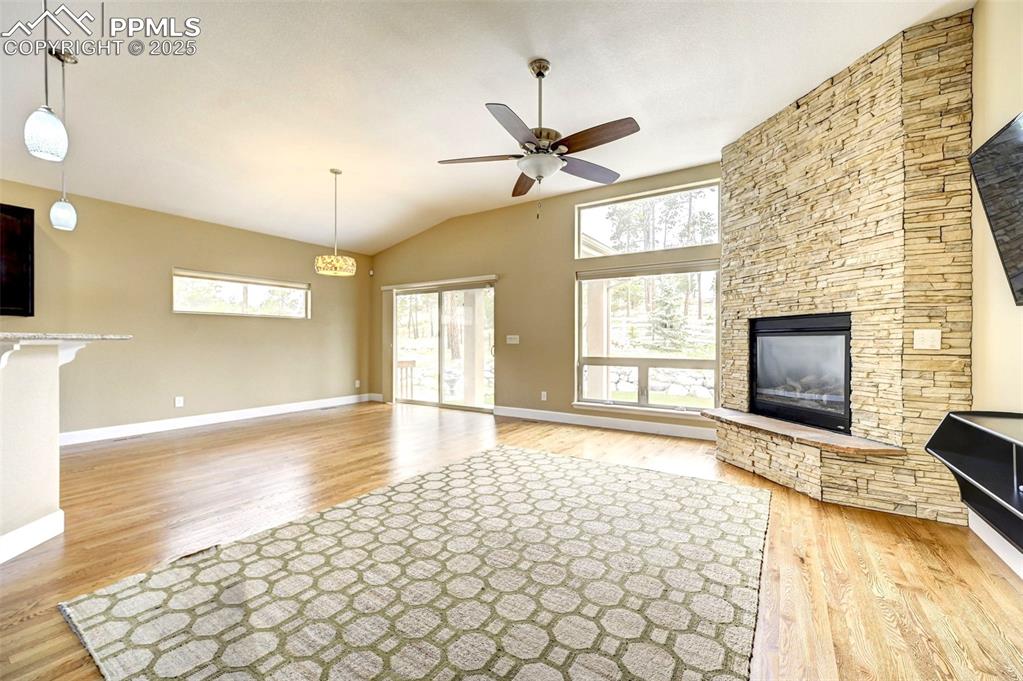 Image 6 of 30: Unfurnished living room with wood finished floors, ceiling fan, a stone fir