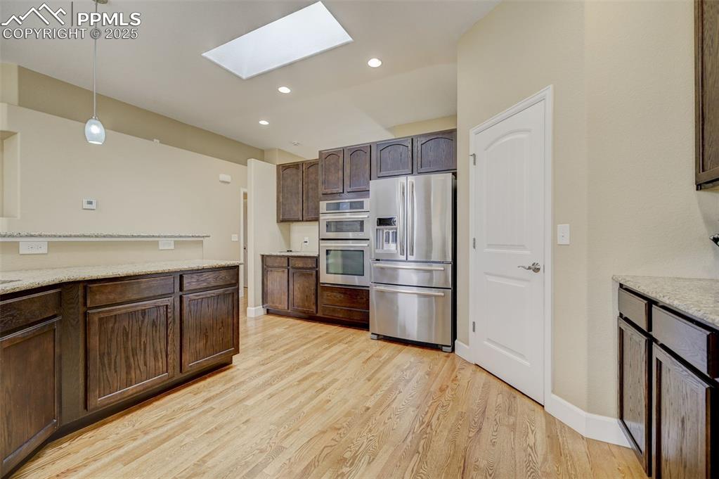 Image 9 of 30: Kitchen with dark brown cabinets, light wood-style floors, hanging light fi