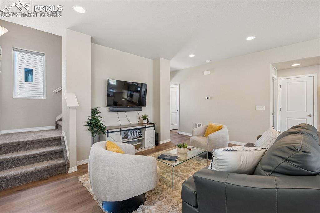 Image 15 of 29: Living area with stairway, wood finished floors, baseboards, and recessed l