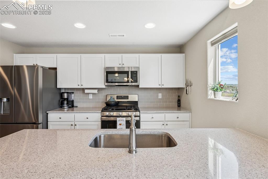 Image 19 of 29: Kitchen featuring stainless steel appliances, white cabinets, decorative ba