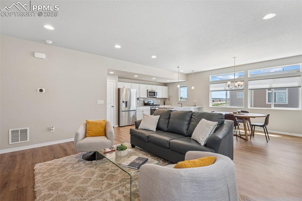 Image 22 of 29: Living room with a chandelier, baseboards, light wood-style flooring, and r
