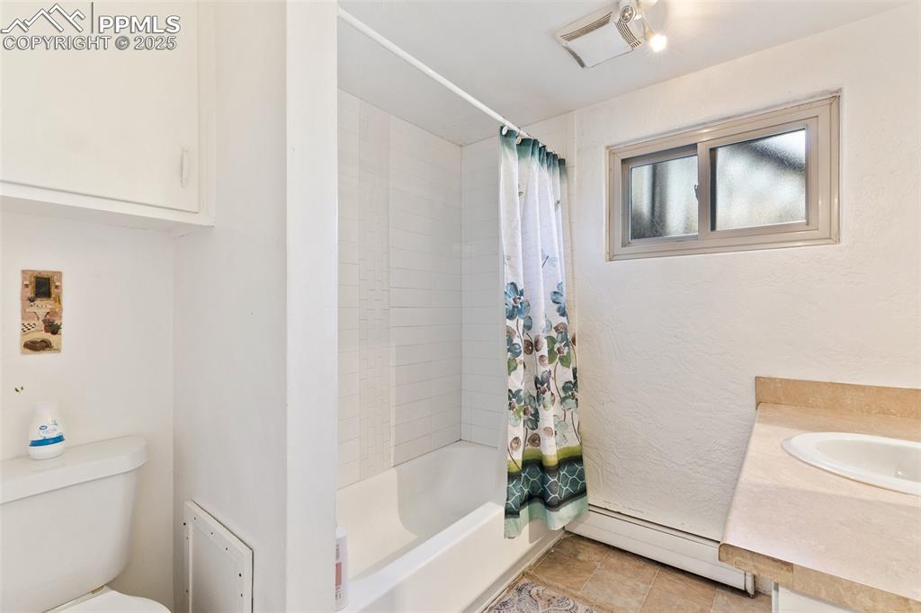 Image 15 of 49: Full bathroom with toilet, shower / bathtub combination with curtain, baseb