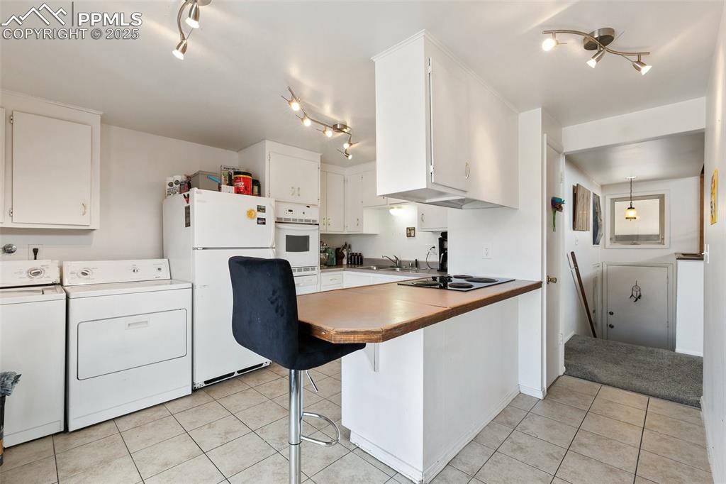 Image 28 of 49: Kitchen with independent washer and dryer, a sink, white cabinetry, white a