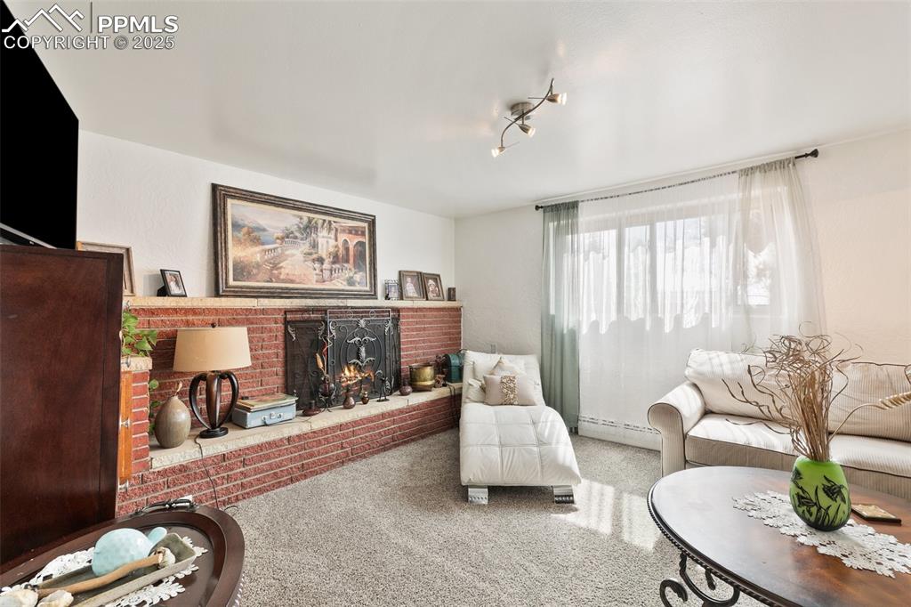Image 4 of 49: Living area featuring a baseboard heating unit, carpet, and a brick firepla