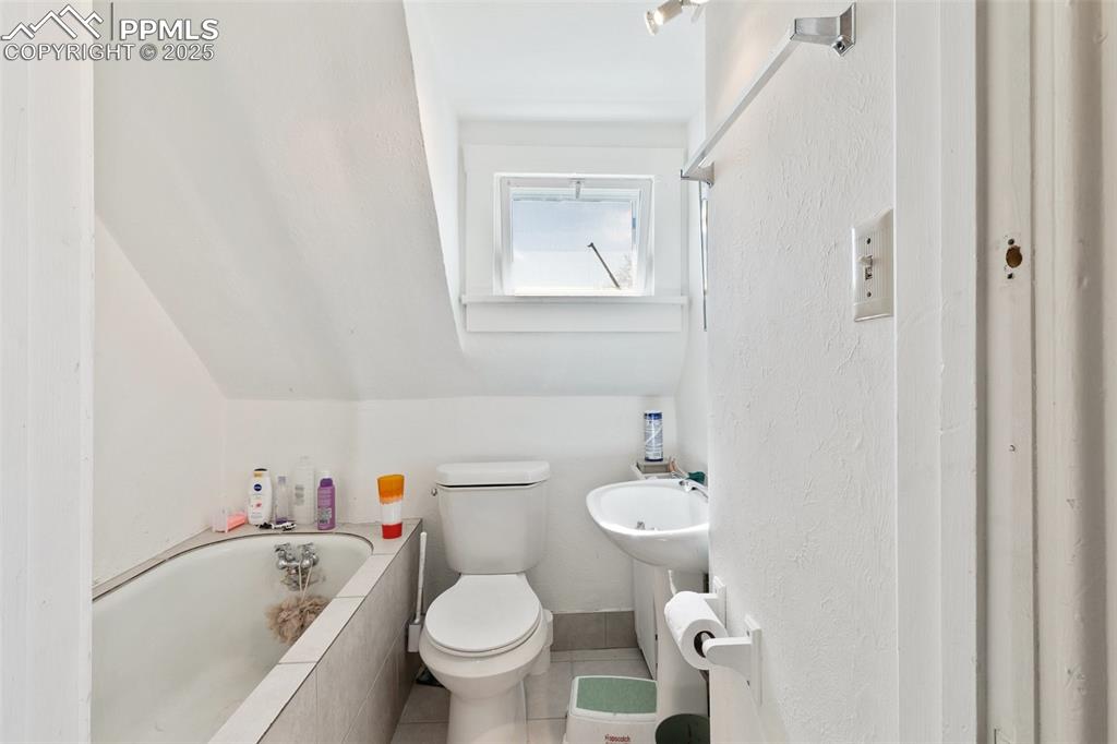 Image 47 of 49: Full bath featuring vaulted ceiling, a relaxing tiled tub, and toilet