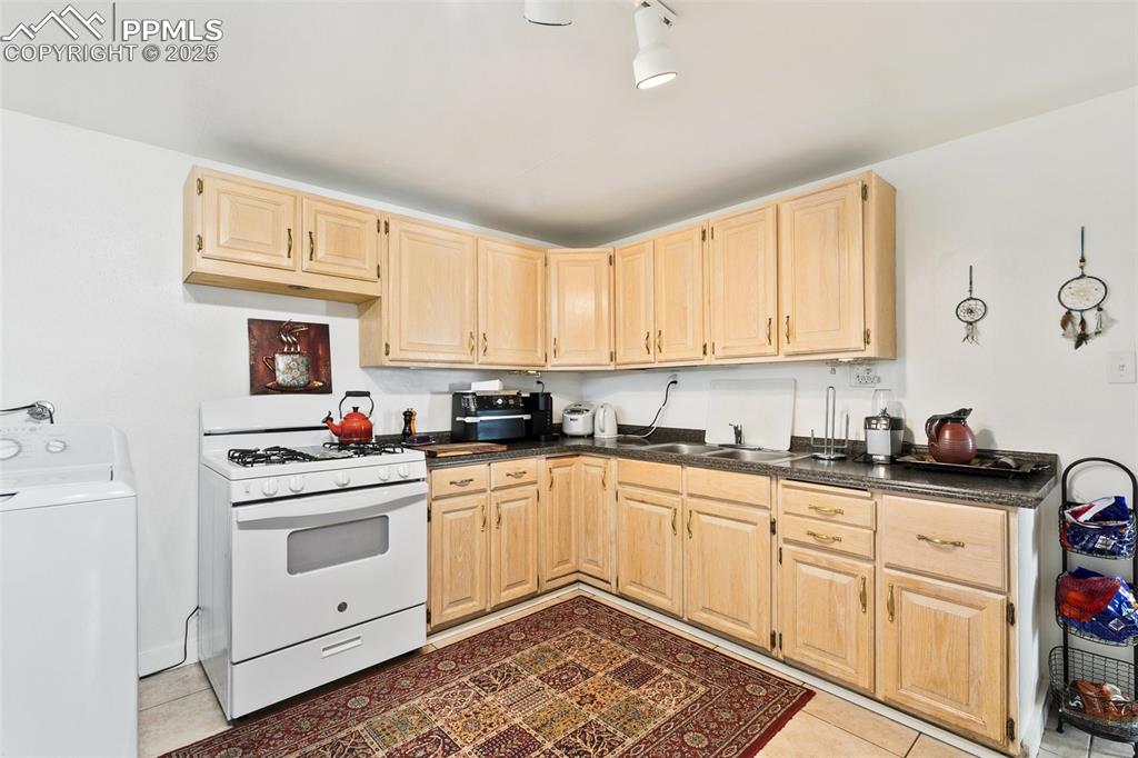 Image 9 of 49: Kitchen featuring white gas stove, light brown cabinetry, dark countertops,