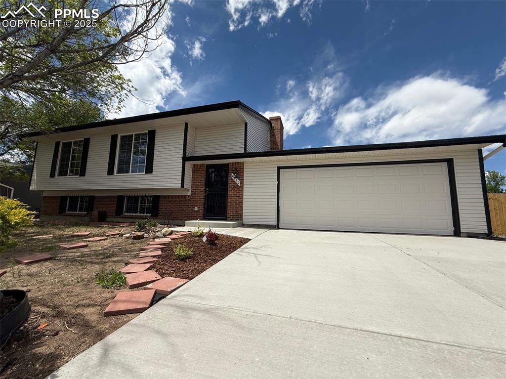 Caption: Split level home with concrete driveway, an attached garage, brick siding, and a chimney