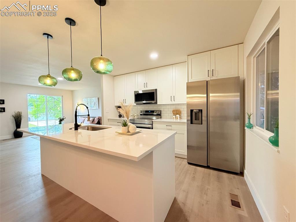 Image 13 of 50: Kitchen with appliances with stainless steel finishes, backsplash, white ca