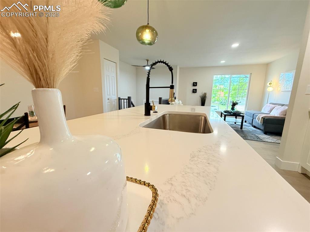 Image 18 of 50: Kitchen with light stone counters, decorative light fixtures, light wood fi