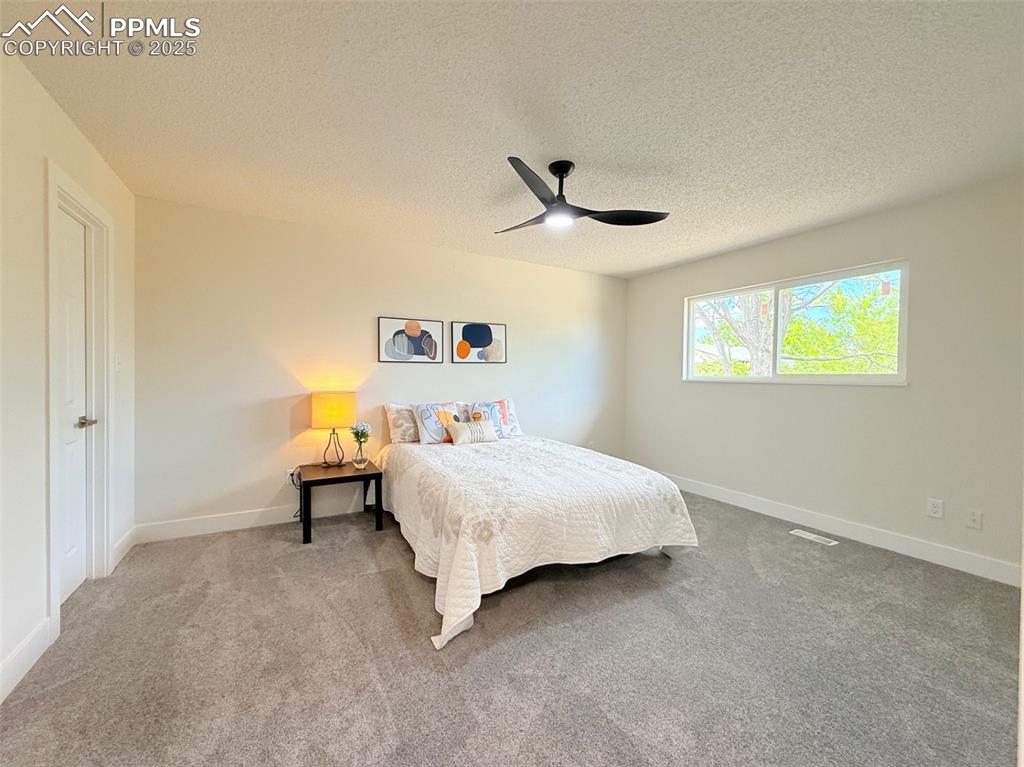Image 21 of 50: Carpeted bedroom with a textured ceiling and ceiling fan