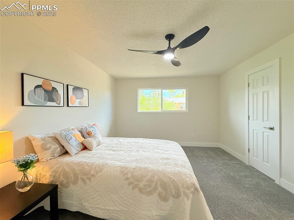 Image 23 of 50: Bedroom featuring a textured ceiling, dark colored carpet, and ceiling fan
