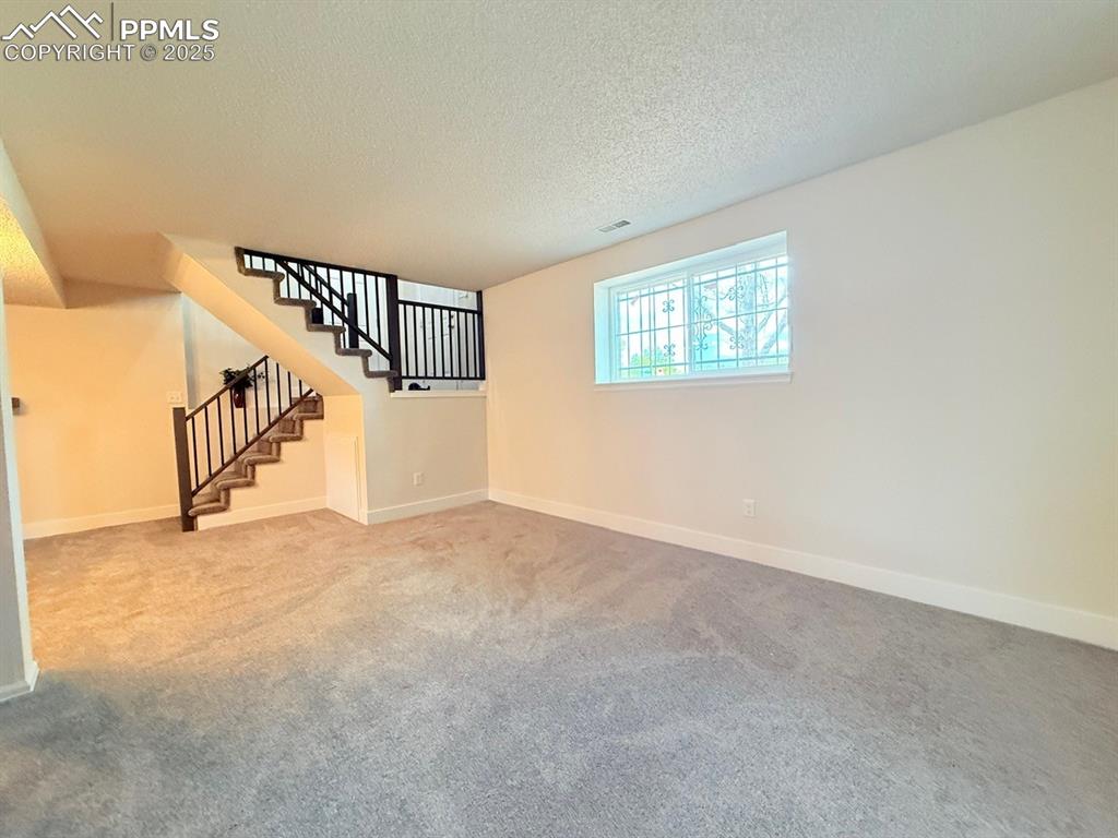 Image 33 of 50: Carpeted spare room with a textured ceiling and stairway