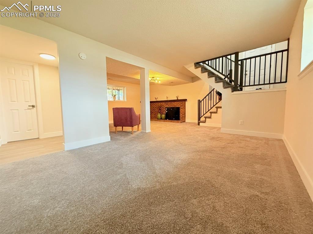 Image 35 of 50: Unfurnished living room with light colored carpet, a fireplace, and stairs