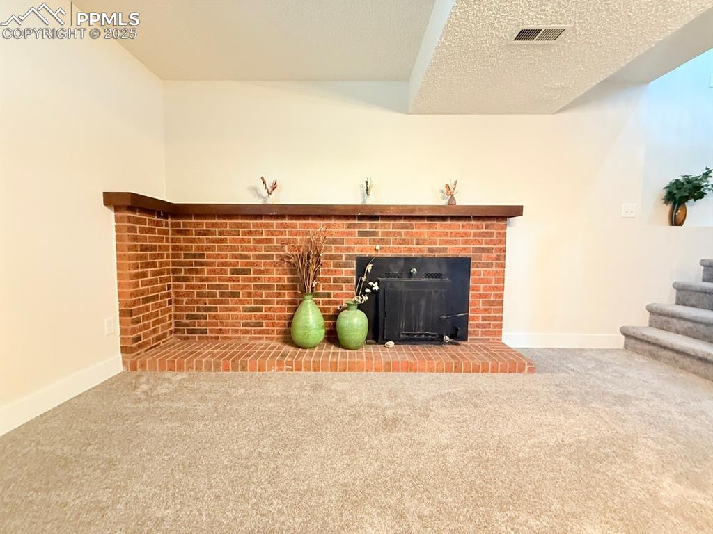 Image 37 of 50: Unfurnished living room featuring carpet, a brick fireplace, and a textured