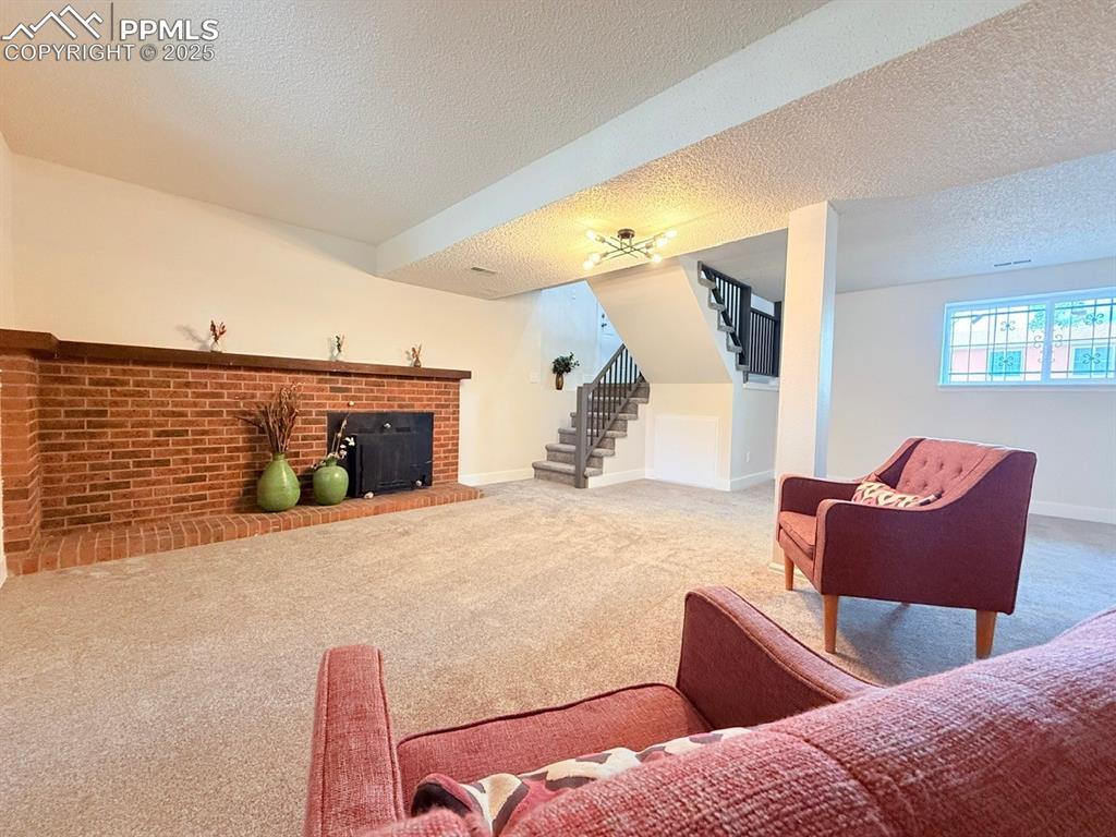 Image 38 of 50: Carpeted living area with stairs, a textured ceiling, and a brick fireplace