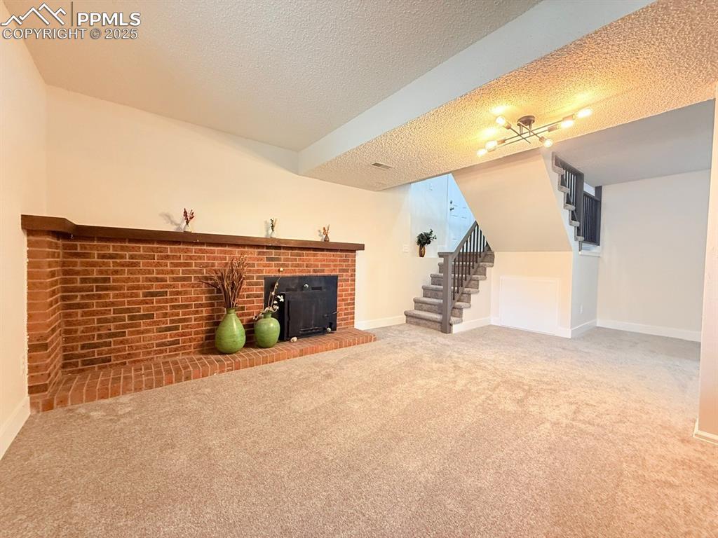 Image 39 of 50: Unfurnished living room featuring stairway, carpet, a textured ceiling, and