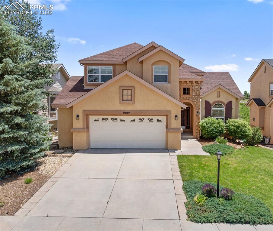 Caption: Traditional-style home with stucco siding, driveway, a front yard, an attached garage, and roof with