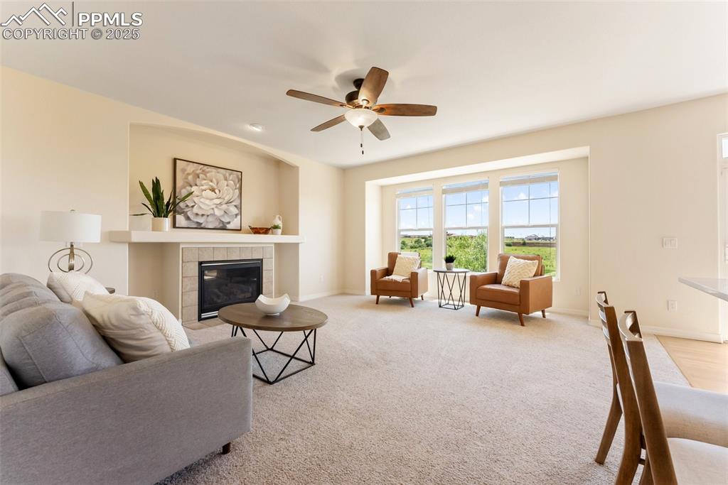 Image 10 of 48: Living area with ceiling fan, a tile fireplace, and carpet flooring