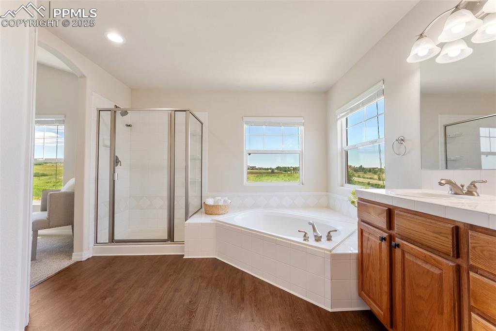 Image 28 of 48: Full bathroom featuring vanity, a bath, a shower stall, and wood finished f