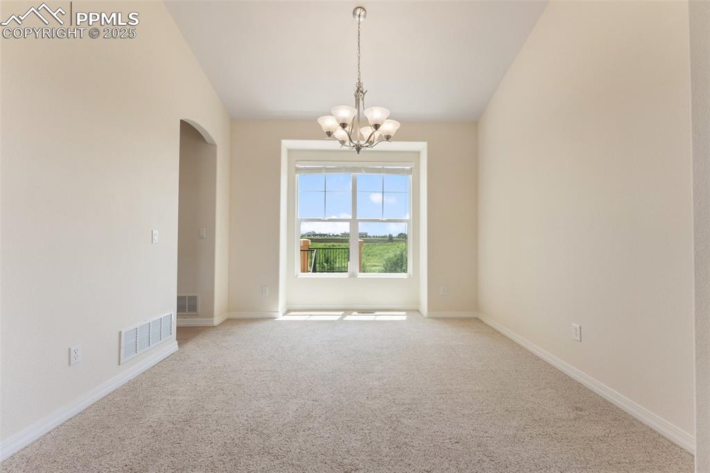 Image 7 of 48: Carpeted spare room featuring arched walkways and a chandelier