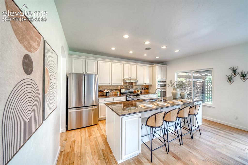 Image 14 of 49: Kitchen featuring wood-finish flooring, white cabinetry, stainless steel ap