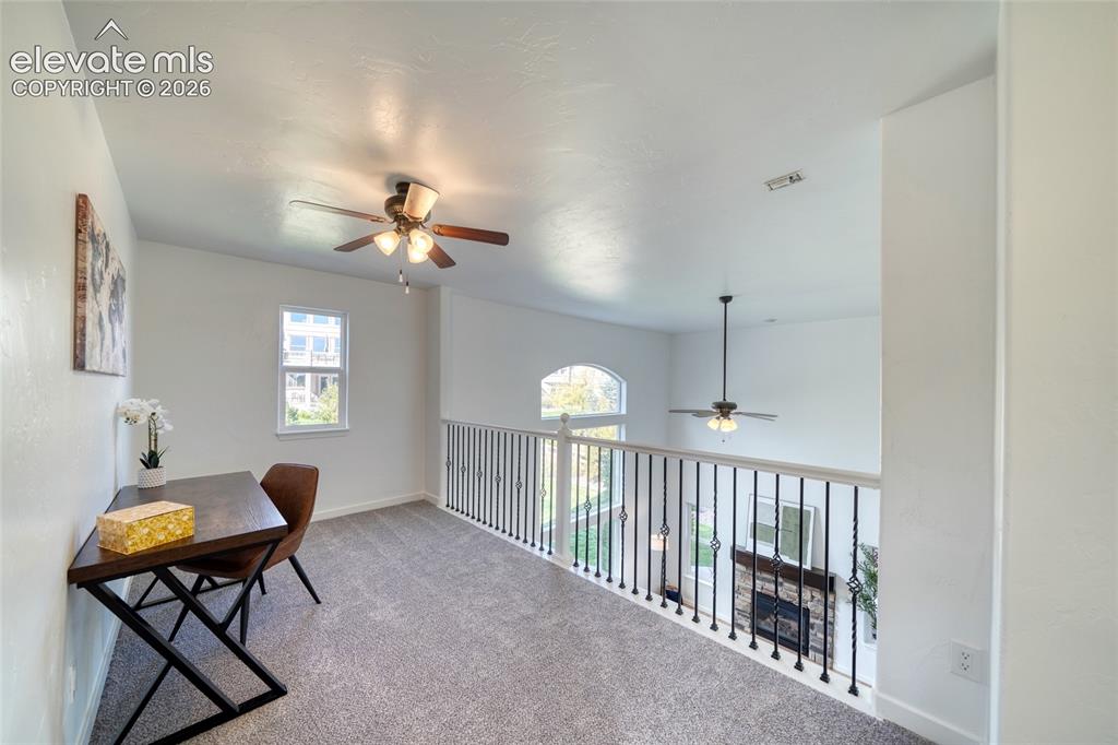 Image 23 of 49: Carpeted open loft area featuring a ceiling fan, a window, and a wrought ir