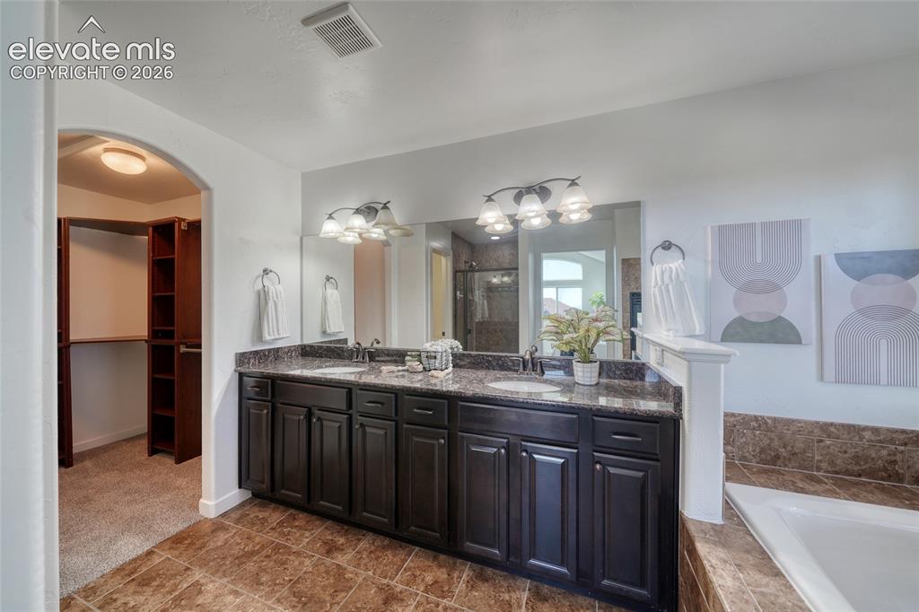 Image 26 of 49: Dual sink vanity with dark wood-finish cabinetry, stone countertop, and til