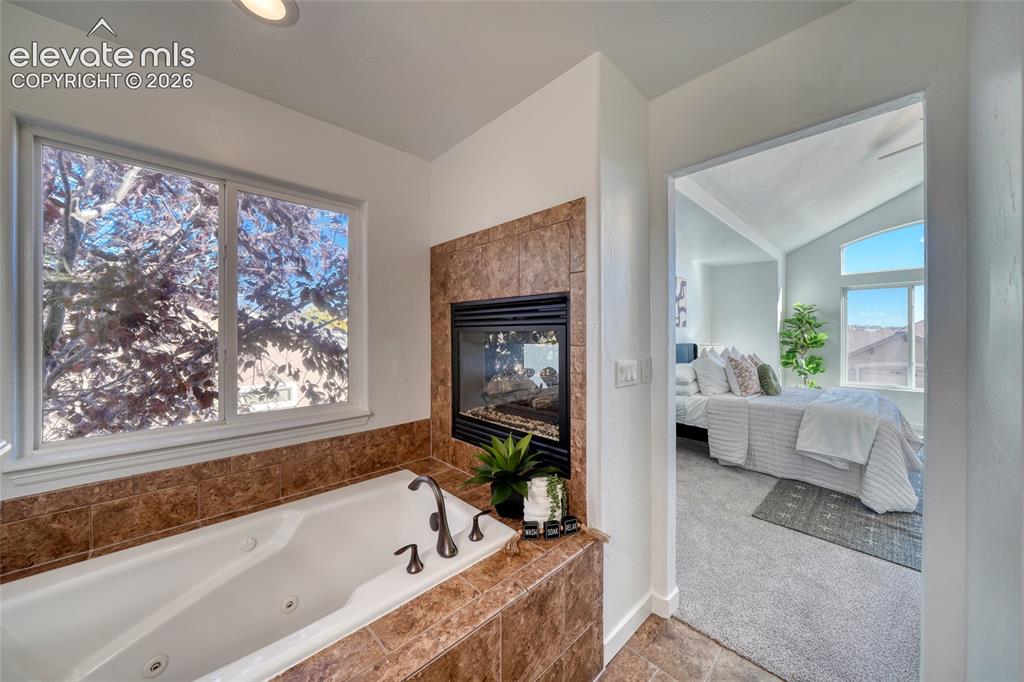 Image 29 of 49: Jetted soaking tub with tile surround, built-in fireplace, and a window
