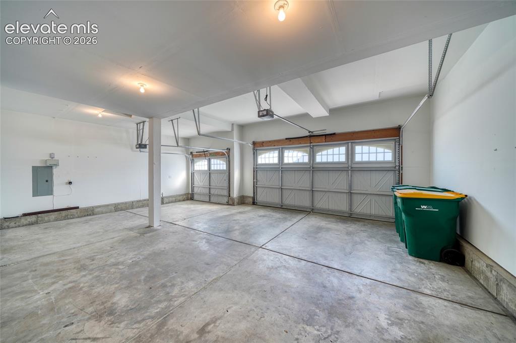Image 36 of 49: Spacious garage with concrete flooring, two overhead doors featuring upper