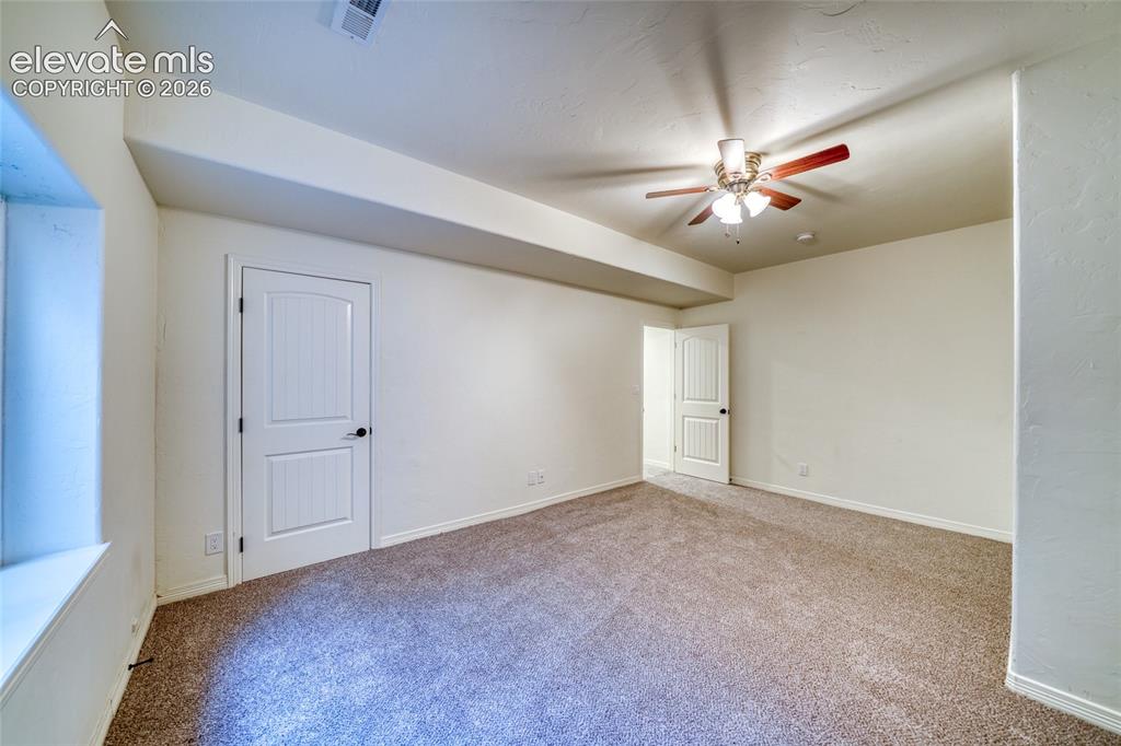 Image 44 of 49: Spacious carpeted room featuring a ceiling fan, white paneled doors, and a 