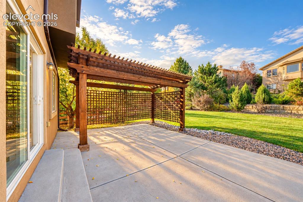 Image 45 of 49: Expansive concrete patio with a wooden pergola, lattice privacy screen, and