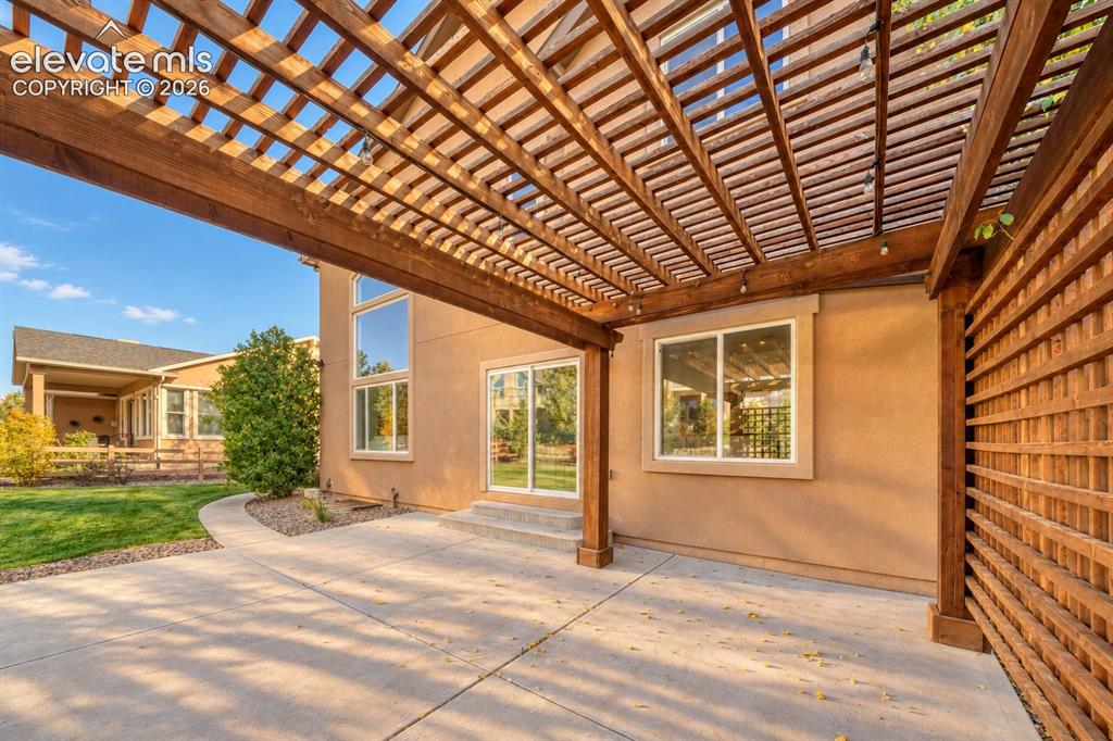Image 46 of 49: Expansive concrete patio with a wooden pergola structure and an adjacent wo