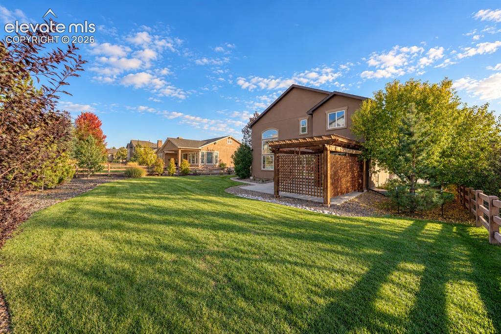 Image 48 of 49: Expansive lawn with mature trees and a wood pergola structure