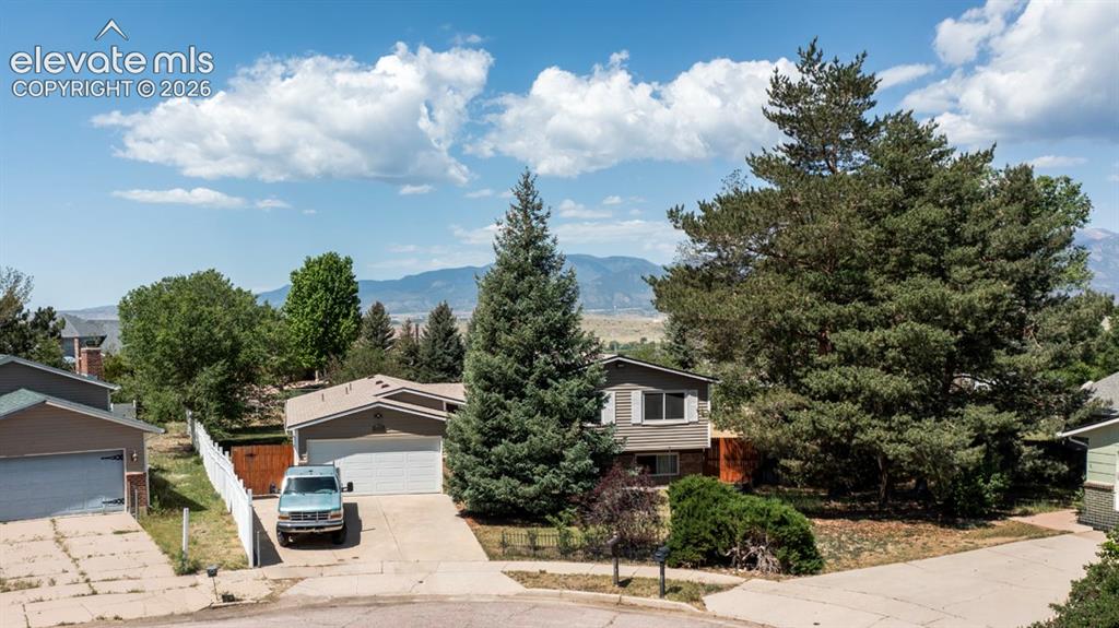 Image 2 of 42: Split-level residence featuring a two-car garage, mature evergreen landscap