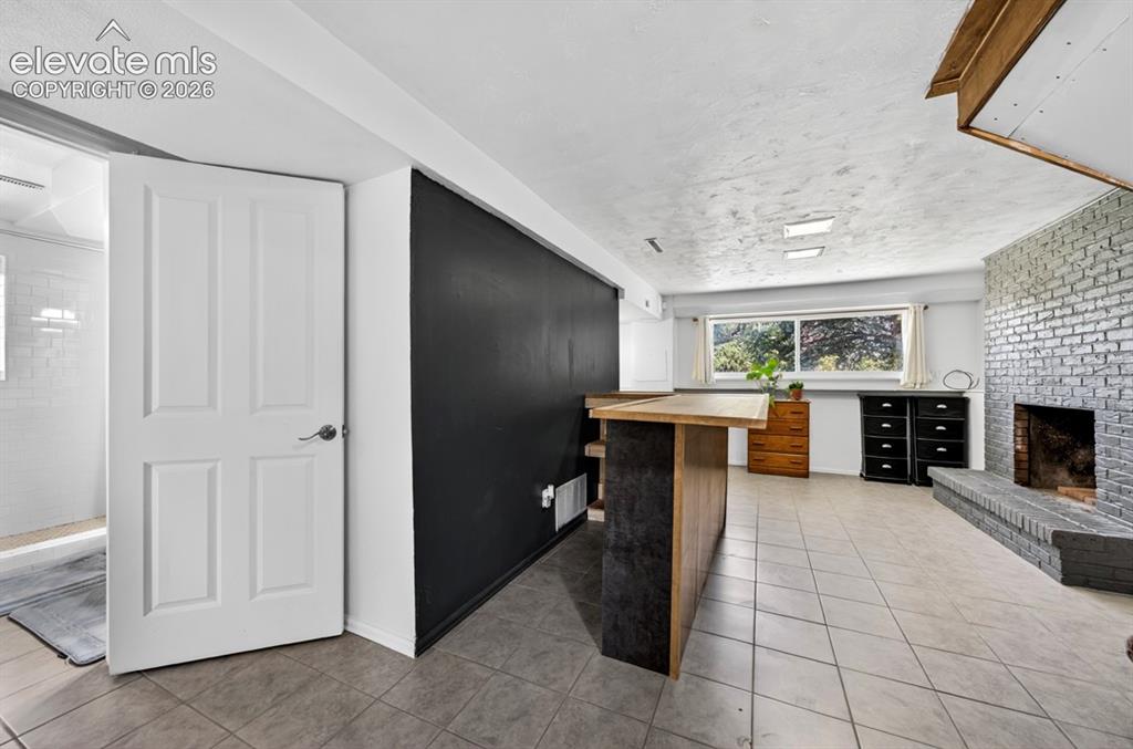 Image 23 of 42: Basement- Spacious lower-level room featuring a fireplace with painted bric