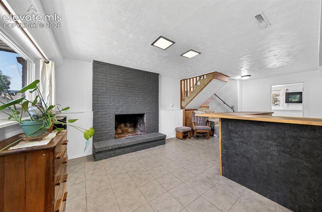 Image 24 of 42: Basement- Open-concept lower level featuring a dark brick fireplace, tiled