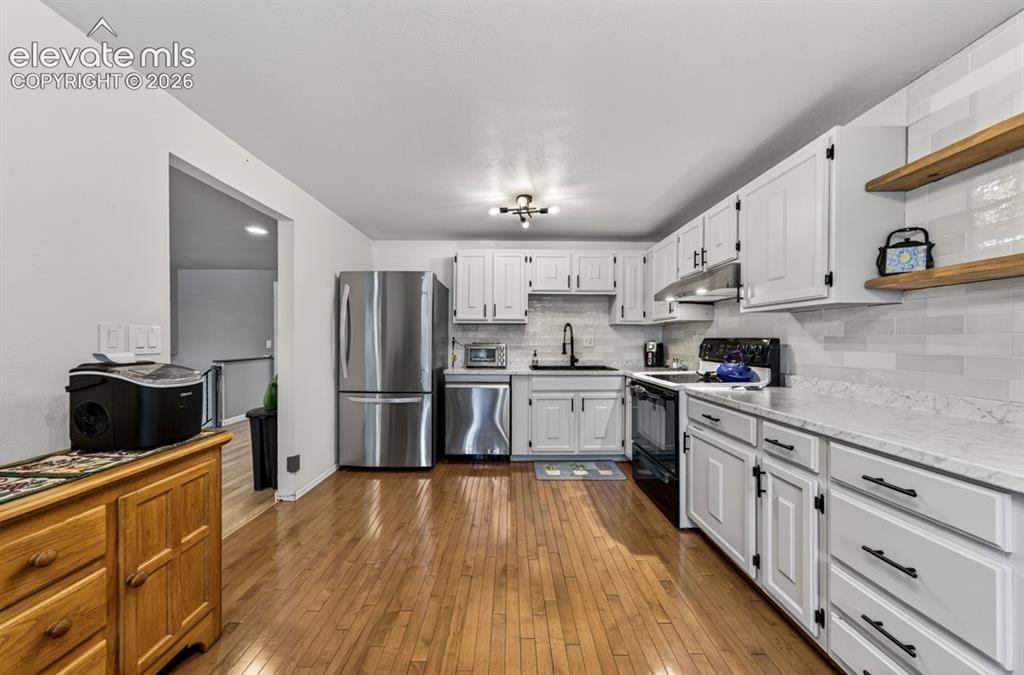 Image 4 of 42: Upper Level- Kitchen featuring wood-finish flooring, white cabinetry with b