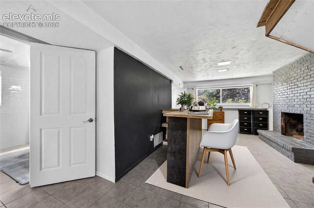 Image 5 of 42: Virtual Staging- Lower-level room with a painted brick fireplace, a custom