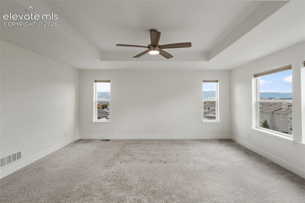 Image 22 of 50: Tray ceiling with a ceiling fan, plush carpeting, and spectacular mountain