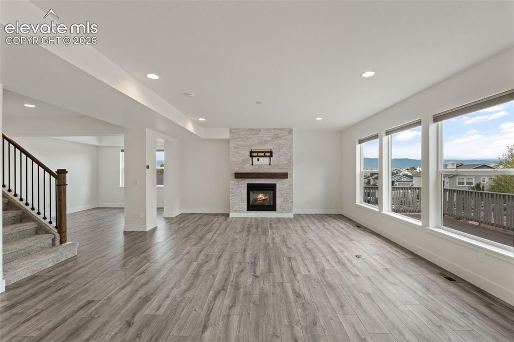 Image 9 of 50: Spacious living area featuring wood-finish flooring, a stone-clad fireplace